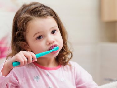 A little girl brushing her teeth in the bathroom.