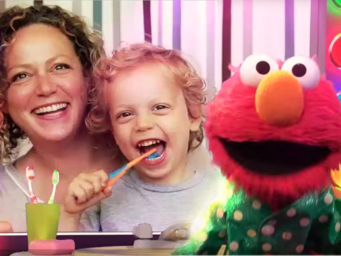 A child brushes their teeth with their parent and Elmo