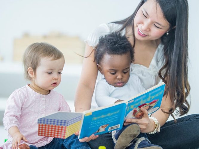 An adult reads a book to two young children.