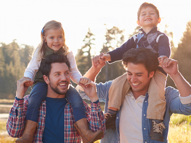 Two adult men each carry a child on their shoulders.