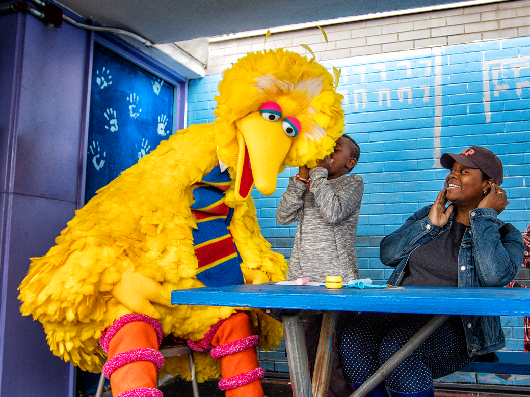 Bird bird at a picnic table as a kid whispers in his ear.
