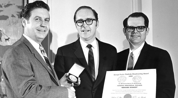 3 men stand with a Peabody award